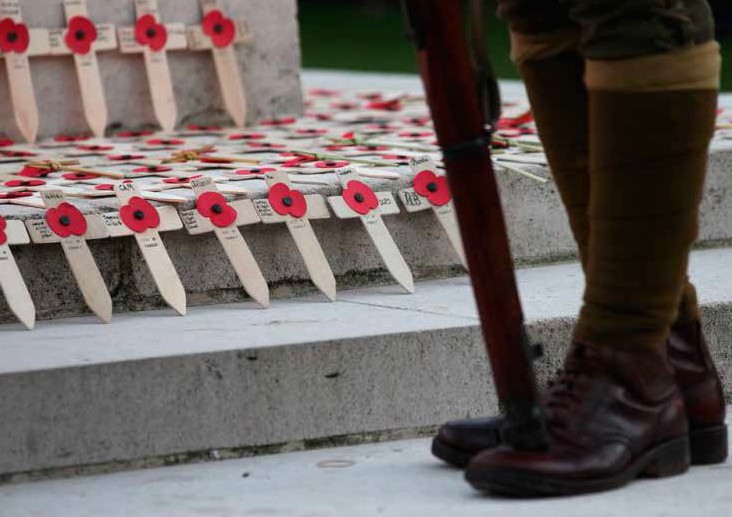 the knees down of a soldier standing at steps that have small crosses with poppies and names on them.